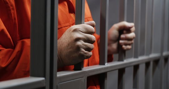 Hands close up of elderly prisoner holding metal bars